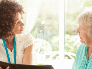 Support worker and elderly woman discussing care plan in a black folder.