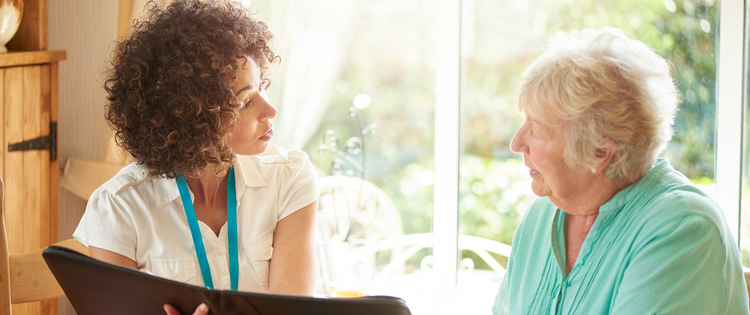 Support worker and elderly woman discussing care plan in a black folder.