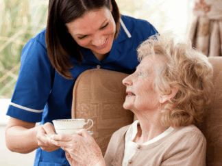 care assistant handing service user a warm drink in a tea cup in a home setting